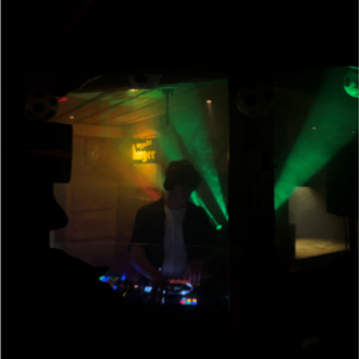 A DJ stands behind a mixing console in a dark room. Colorful beams of light create a vibrant atmosphere.