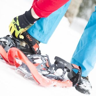 Eine Person schnallt Schneeschuhe an, während sie auf dem weißen Schnee steht. Der Hintergrund ist unscharf, was auf einen winterlichen Wald hinweist. | © Kleinwalsertal Tourismus | Oliver Farys
