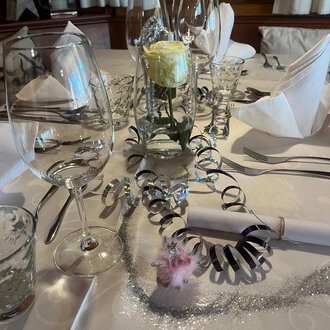 Zwei Sektgläser stoßen auf einem festlich dekorierten Tisch an. Im Hintergrund sind rote Weihnachtskugeln und goldene Dekoration zu sehen. | © Genuss- & Aktivhotel Sonnenburg