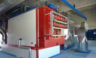 A modern industrial facility with large machines and pipes. The main machine is red and white, surrounded by a structured environment.