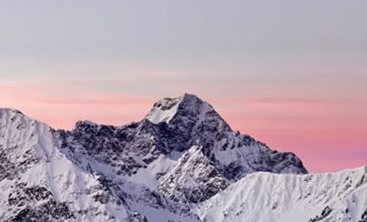 A majestic mountain landscape with snow-capped peaks and a soft pink sky. The scene exudes tranquility and natural beauty.