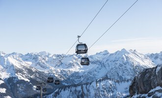 Eine Seilbahn fährt über schneebedeckte Berge. Der Himmel ist klar und blau, die Landschaft ist beeindruckend. | © OBERSTDORF · KLEINWALSERTAL BERGBAHNEN