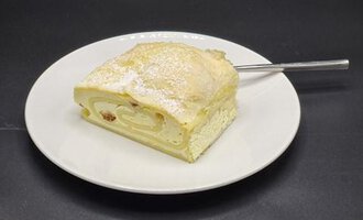 Ein Stück Biskuitrolle auf einem weißen Teller. Der Kuchen ist mit Puderzucker bestäubt und hat eine Füllung.