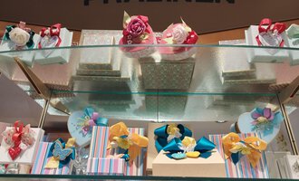 An elegant shelf with beautifully packaged chocolates in various colors and shapes. The packaging is lovingly adorned with ribbons and decorations. | © Kleinwalsertal Tourismus | N. Lughammer