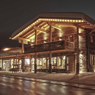Ein gemütliches Holzgebäude mit warmem Licht in der Nacht. Der schneebedeckte Boden und das stilvolle Design schaffen eine einladende Atmosphäre. | © Fun-Alp