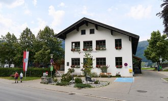Ein charmantes Gemeindegebäude mit blühenden Blumenkästen. Im Hintergrund sind weitere Gebäude und Bäume zu sehen. | © Kleinwalsertal Tourismus | Oliver Farys