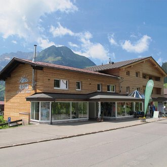 A modern wooden building in the mountains. Surrounded by a beautiful landscape with green forests and mountains. | © Sport Hilbrand GmbH