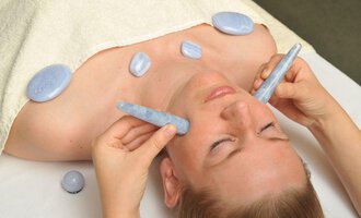A woman is receiving a relaxing facial treatment with blue stones. Her eyes are closed while her skin is being pampered. | © Bio-Hotel Oswalda Hus | Joachim Weiler