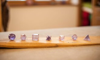 A series of octagonal and geometric crystals in various shapes and sizes. The crystals are arranged on a wooden board in gentle shades of purple. | © Bio-Hotel Oswalda Hus | Joachim Weiler