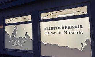 Eine Tierarztpraxis mit dem Namen "KLEINTIERPRAXIS Alexandra Hirschel". Die Fenster zeigen Silhouetten von Hund, Katze und Kaninchen.