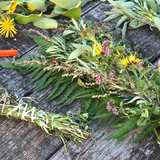 Ein Tisch mit frischen Kräutern und bunten Blumen. Jemand bindet einen Kräuterkranz mit einer Schere daneben. | © Kleinwalsertal Tourismus | Lydia Fritz-Ilg