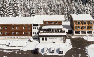 A snow-covered landscape with several buildings in chalet style. Surrounded by tall, snow-covered fir trees. | © Marburger Haus | Sweetchili