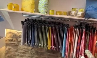 A beautiful gift shop with colorful cushions and a shelf full of scarves. On the table, there are various decorative items and cups. | © Herzstichle | Ninja Matt