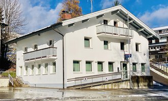 A modern, three-story building with white walls and green windows. It is located in a quiet environment with light snowfall. | © Polizeiinspektion Kleinwalsertal | C. Zwerger