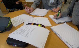 Eine Gruppe von Menschen sitzt an einem Tisch und arbeitet an Dokumenten. Schreiben, Notizen und Schreibmaterialien sind gut sichtbar. | © Kleinwalsertal Tourismus