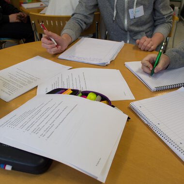 A group of people is sitting at a table and working on documents. Writing, notes, and writing materials are clearly visible. | © Kleinwalsertal Tourismus
