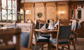 Ein gemütliches Restaurant mit Holzwänden und eleganten Tischdekorationen. Die Stühle sind mit blauen Stoffen bezogen und vermitteln eine einladende Atmosphäre.