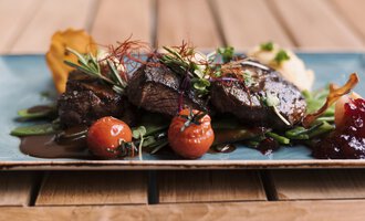 Ein köstliches Gericht mit saftigem Fleisch, verfeinert mit Kräutern und frischen Tomaten. Dazu gibt es eine beeindruckende Anrichtung auf einem eleganten Teller.
