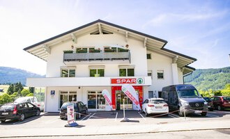 A modern commercial building with the Spar logo in the foreground. Numerous cars are parked in the parking lot in front of the door. | © SPAR