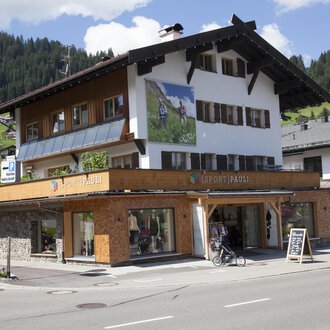 A charming building with traditional architecture, surrounded by mountains. On the ground floor, there is a shop with large windows. | © Sport Pauli Matthias Bischof e.U