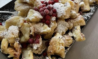 Ein Teller mit gebackenem Teig, bestreut mit Puderzucker und roten Beeren. Dazu gibt es eine Schale Apfelmus. | © Uusziit | Chantal Kessler