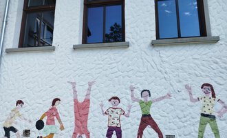Eine bunte Wandmalerei zeigt Kinder in verschiedenen Spielpositionen. Sie fröhlich freundlich und lebhaft aus. | © Kleinwalsertal Tourismus | N. Lughammer
