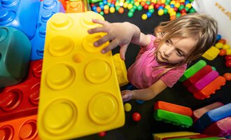 A small child is playing with large, colorful building blocks in a play area. They are holding a yellow block in their hand and seem to be focused. | © Wonniland Sonthofen | interSPA Gruppe