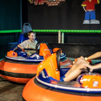Zwei Kinder fahren mit elektronischen Bumper Cars in einer Sporthalle. Eines der Kinder hat einen Ausdruck voller Freude und Aufregung im Gesicht. | © Wonniland Sonthofen | interSPA Gruppe