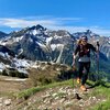 Woman hiking in the mountains with snow-capped peaks, carrying a backpack and trekking poles on a sunny day. | © Kleinwalsertal Tourismus eGen