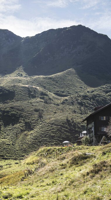 A house on green hills in the Black Water Valley, surrounded by mountains on a clear day. | © Kleinwalsertal Tourismus eGen • Photographer: Andre Tappe
