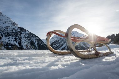 Sleds on snow with mountains and sunlight shining through in a winter landscape. | © Kleinwalsertal Tourismus eGen • Photographer: Dominik Berchtold