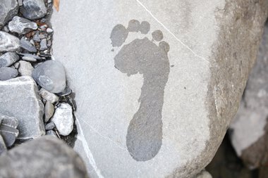A close-up of a stone with a natural footprint, surrounded by small stones and gravel. | © Kleinwalsertal Tourismus eGen • Photographer: Frank Drechsel