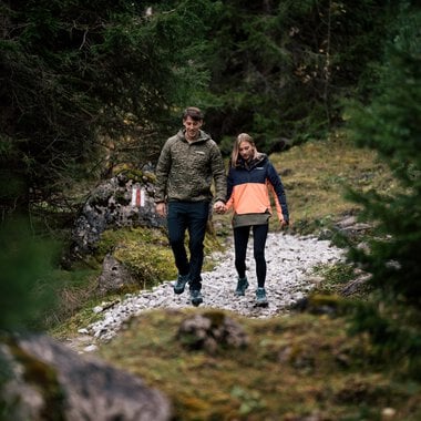 Ein Paar wandert Hand in Hand durch einen bewaldeten Pfad in der Natur bei Tageslicht. | © Kleinwalsertal Tourismus eGen • Fotograf: Hannah Bichay
