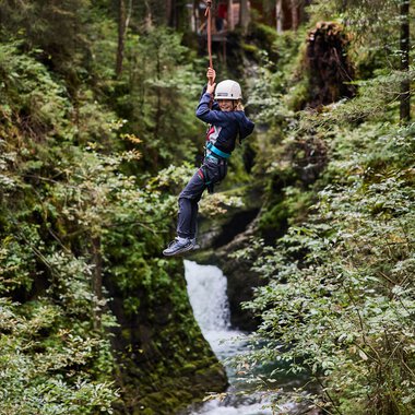 Child ziplining over a stream in a lush green forest in Kleinwalsertal. | © Kleinwalsertal Tourismus eGen • Photographer: Oliver Farys