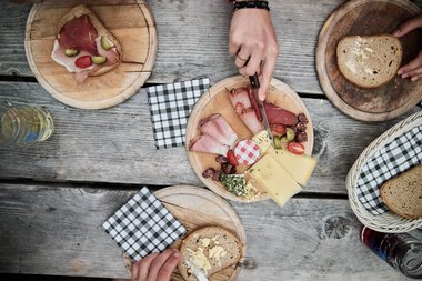 Frühstückstisch mit verschiedenen Brotsorten, Käse, Aufschnitt und Getränken auf einer Holztafel bei einer Wanderung im Kleinwalsertal. | © Kleinwalsertal Tourismus eGen • Fotograf: Oliver Farys