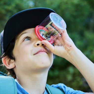 Junge Naturforscher mit Kinderlupe in der Hand, in einer grünen Waldumgebung. | © Kleinwalsertal Tourismus eGen • Fotograf: Oliver Farys