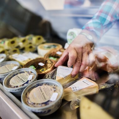 Hand wählt Käse im Käsefach eines Verkaufsstands beim Walser Wochenmarkt im Kleinwalsertal. | © Kleinwalsertal Tourismus eGen • Fotograf: Oliver Farys