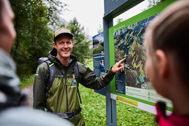 Ein Mann erklärt einer Gruppe von Kindern eine Karte im Kleinwalsertal, um Wissensvermittlung im Naturschutzgebiet | © Kleinwalsertal Tourismus eGen • Fotograf: Oliver Farys