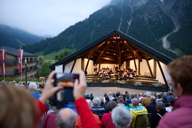 Public outdoor concert on a stage in a mountain village with a large audience enjoying the summer event. | © Kleinwalsertal Tourismus eGen • Photographer: Oliver Farys