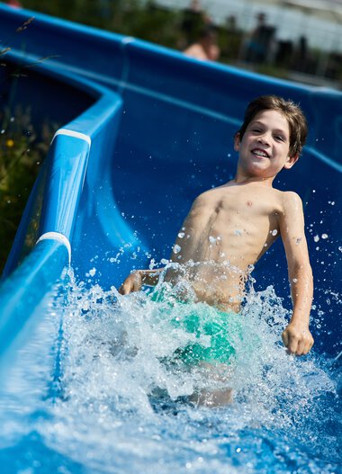 Boy happily sliding down a water slide at Freibad Riezlern in Kleinwalsertal. | © Kleinwalsertal Tourismus eGen • Photographer: Oliver Farys