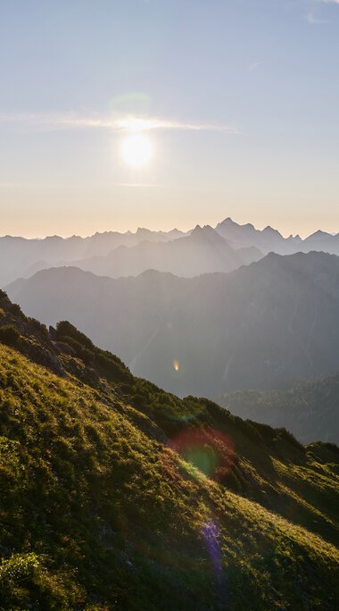 Landscape in Kleinwalsertal at sunset, with mountains and green hills in the foreground. | © Kleinwalsertal Tourismus eGen • Photographer: Oliver Farys