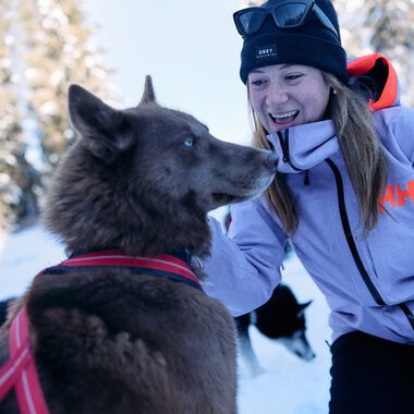 Woman in winter gear playing with a husky in a snowy winter landscape. | © Kleinwalsertal Tourismus eGen • Photographer: Oliver Farys