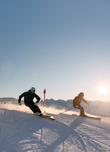 Two skiers racing down a snowy slope in sunlight at Kleinwalsertal, Austria. | © Kleinwalsertal Tourismus eGen • Photographer: Oliver Farys