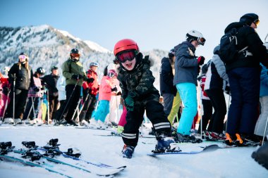 A young boy skiing and smiling, surrounded by other skiers in a snowy mountain landscape. | © Kleinwalsertal Tourismus eGen • Photographer: Oliver Farys
