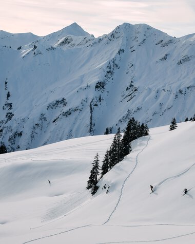 Snowy mountain landscape with ski tracks and skiers in Kleinwalsertal, featuring stunning views of snowy peaks and mountains. | © Kleinwalsertal Tourismus eGen • Photographer: Oliver Farys