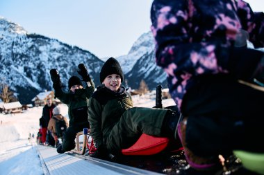 Children sledding in the snow in the mountains, laughing and playing, winter vacation in Kleinwalsertal. | © Kleinwalsertal Tourismus eGen • Photographer: Oliver Farys