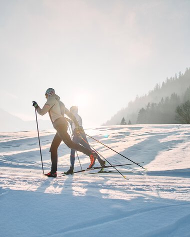 Two cross-country skiers on the Schwarzwasserloipe in Kleinwalsertal during sunrise. | © Kleinwalsertal Tourismus eGen • Photographer: Oliver Farys