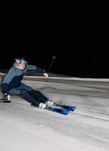 Night skiing in Kleinwalsertal, a skier making a sharp turn on the snow against a dark night sky. | © Kleinwalsertal Tourismus eGen • Photographer: Oliver Farys