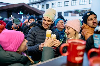 Menschen beim Schneemann-Treffen im Kleinwalsertal, lachen und trinken warme Getränke an einem verschneiten Tag | © Kleinwalsertal Tourismus eGen • Fotograf: Oliver Farys