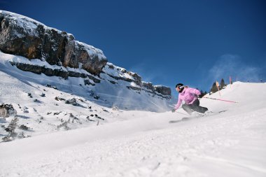 Skier skiing downhill on a snowy slope in Kleinwalsertal, with rocks in the background and clear blue sky. | © Kleinwalsertal Tourismus eGen • Photographer: Oliver Farys